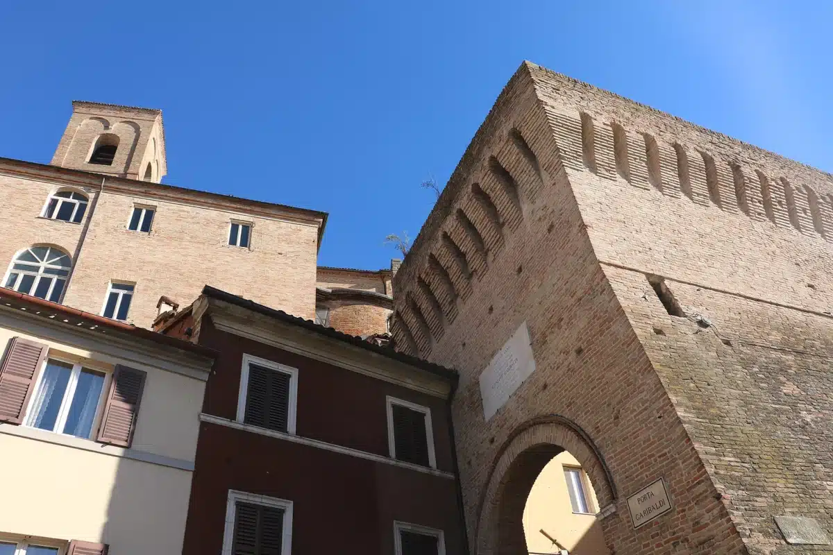 Medieval brick city walls of Jesi with a gate arch and arched corbels along the top