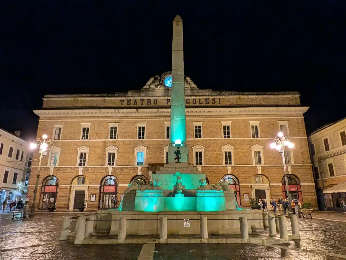 Teatro Pergolesi in Jesi at night with the lit obelisk of the Fontana dei Leoni in front